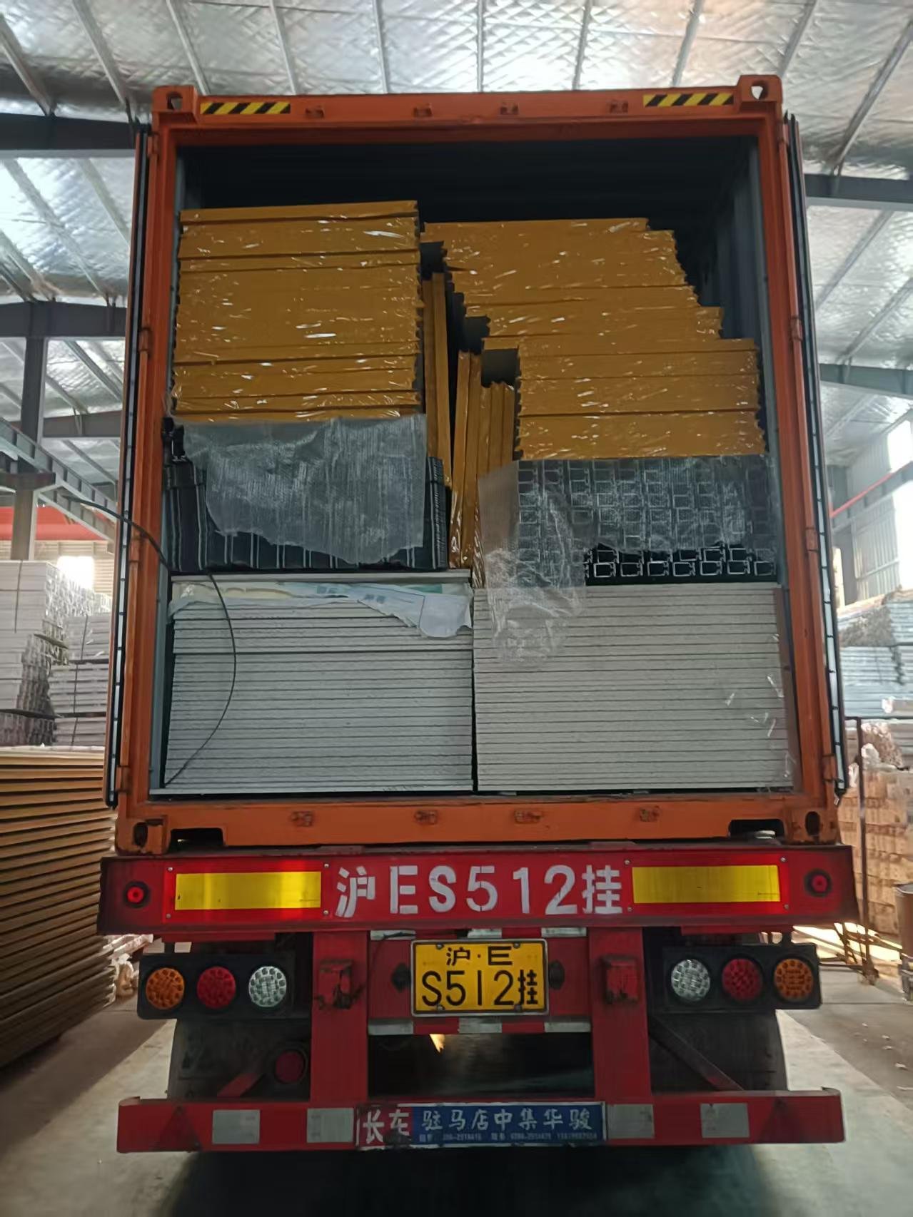 Stacked wall panels and bundled steel sections loaded into a shipping container for flat pack houses